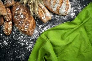 Different bread with flour and spikelets of wheaton black background photo