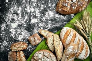 Different bread with flour and spikelets of wheaton black background photo