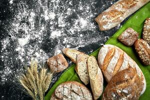 Different bread with flour and spikelets of wheaton black background photo