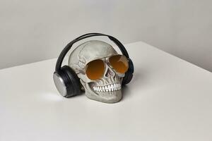 Realistic model of a human skull with teeth in a sunglasses and headphones on a light table, white background. Medical science or Halloween horror concept. photo