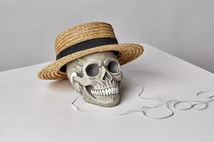Realistic model of a human skull with teeth in a yellow straw hat and headphones on a light table, white background. Halloween horror concept. photo