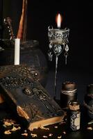 Books with spells, old pot, jars of potion are on a wooden dark table. Petals of dried roses are scattered nearby. Black background. Close-up shot. photo