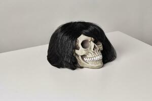 Realistic model of a human skull with teeth in a black wig on a light table, white background. Medical science or Halloween horror concept. photo