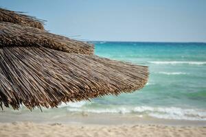 Close-up shot of a straw umbrella standing at the beach of the azure mediterranean sea, surrounded by a beautiful nature of Cyprus. Ayia Napa. photo