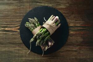 An edible, raw stems of asparagus on a wooden background. photo