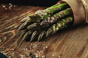 An edible, raw stems of asparagus on a wooden background. photo