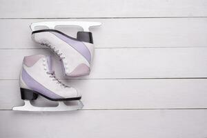 Close-up photo of professional ice skates lying on a white wooden background.