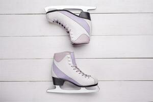 Close-up photo of professional ice skates lying on a white wooden background.