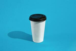 Hot coffee in white paper cup with black lid on blue background photo