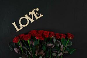 Red roses flowers with wooden word LOVE on black background with photo