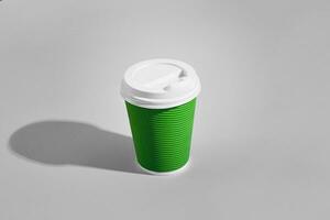 Hot coffee in green paper cup with white lid on gray background photo