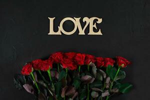 Red roses flowers with wooden word LOVE on black background with photo