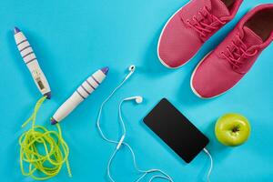 Flat lay shot of Sport equipment. Sneakers, jump rope, earphones and phone on blue background. photo