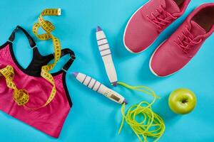 Flat lay of female sport equipments in pink color with jump rope and sneakers on blue background photo