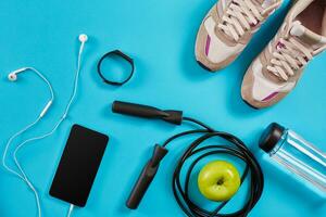 Flat lay shot of Sport equipment. Sneakers, jump rope, earphones and phone on blue background. photo