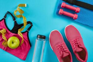 Sneakers with measuring tape on cyan blue background. Centimeter in yellow color, pink sneakers, female sport top and bottle of water, copy space. photo