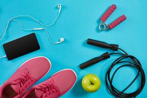 Flat lay shot of sneakers, jumping rope, dumbbells and smartphone on blue background. photo