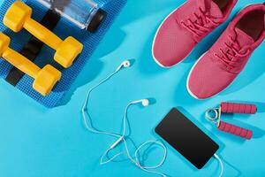 Flat lay shot of Sport equipment. Sneakers, water, earphones and phone on blue background. photo