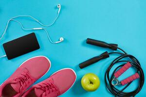 Flat lay shot of sneakers, jumping rope, dumbbells and smartphone on blue background. photo