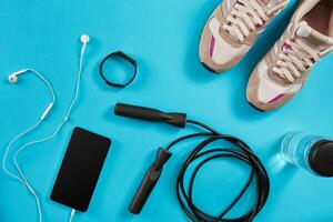 Flat lay shot of Sport equipment. Sneakers, jump rope, earphones and phone on blue background. photo