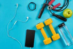 Dumbbells, mobile phone and skipping rope on blue background. Top view. Fitness, sport and healthy lifestyle concept. photo