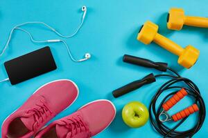 Flat lay shot of sneakers, jumping rope, dumbbells and smartphone on blue background. photo