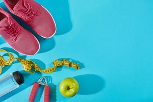 Sneakers with measuring tape on cyan blue background. Centimeter in yellow color near pink trainers, close up. photo