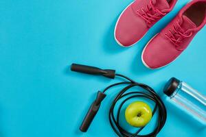 Flat lay of female sport equipments, jump rope, bottle of water and pink sneakers on blue background photo