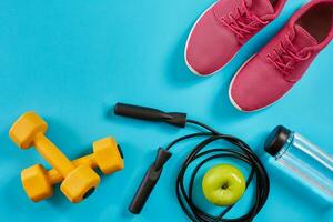 Flat lay of female sport equipments, jump rope, bottle of water and pink sneakers on blue background photo