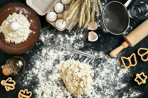 Cooking dough for cookies, butter, eggs, cooking equipment, flour on a black table. Top view with copy space, mockup for menu, recipe or culinary classes. Baking background. photo