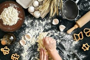 Woman's hands knead dough on table with flour, eggs and ingredients. Top view. photo