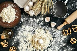 Cooking dough for cookies, butter, eggs, cooking equipment, flour on a black table. Top view with copy space, mockup for menu, recipe or culinary classes. Baking background. photo