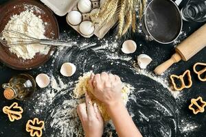 Woman's hands knead dough on table with flour, eggs and ingredients. Top view. photo