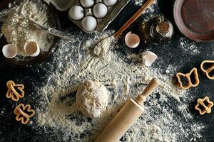 Cooking dough for cookies, butter, eggs, cooking equipment, flour on a black table. Top view with copy space, mockup for menu, recipe or culinary classes. Baking background. photo