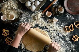 Female hands rolling dough with a rolling pin on a black table. Top view photo