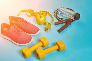 Flat lay of dumbbell, bottle of water, jump rope and sneaker, sport equipments, fitness items, top view. Sun flare photo