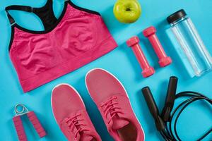 Athlete's set with female clothing, dumbbells and bottle of water on bright blue background photo