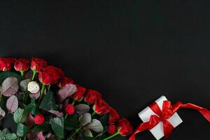 Red roses and white gift box with red ribbon on black background photo