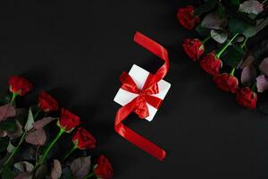 Red roses, ring and gift box on black background photo