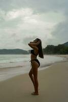 Gorgeous brunette woman with perfect figure posing on  tropical  beach. Wearing stylish black swimwear. photo