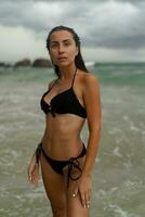 Gorgeous brunette woman with perfect figure posing on  tropical  beach. Wearing stylish black swimwear. photo