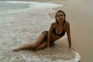 Romantic woman in  black swimsuit laying on a beach in the water at the sea. Seductive  girl in bikini resting during summer vacation at the seashore photo