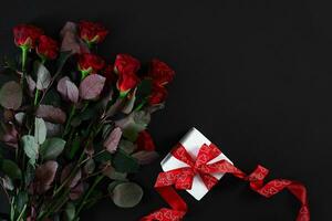 Red roses, ring and gift box on black background photo