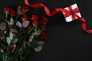 Red roses, ring and gift box on black background photo