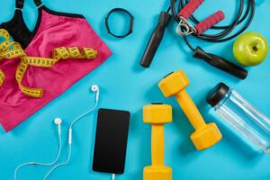 Athlete's set with female clothing, dumbbells and bottle of water on bright blue background photo
