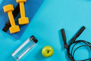 Dumbbells, bottle of water and skipping rope on blue background. Top view. Fitness, sport and healthy lifestyle concept. photo