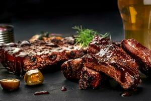 Pork ribs in barbecue sauce and a glass of beer on a black slate dish. A great snack to beer on a dark stone background. Top view with copy space photo