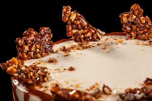 Round white cake with caramel and chocolate puffed rice on a round tray on black background photo