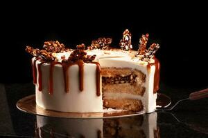 Round white cake with caramel and chocolate puffed rice on a round tray on black background photo