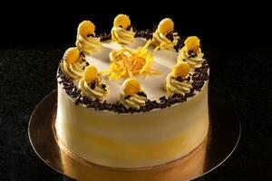 Round yellow birthday cake. Decorative cream decorations on the cake. Black background. photo